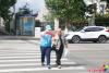 9月18日，在延吉市局子街北大市場(chǎng)西側(cè)的十字路口旁，大學(xué)志愿者劉書(shū)達(dá)頭戴志愿者標(biāo)志帽、身穿藍(lán)馬甲、佩戴綬帶和袖標(biāo)，手拿小紅旗，在路口維護(hù)交通秩序，引導(dǎo)行人通過(guò)斑馬線安全過(guò)馬路。